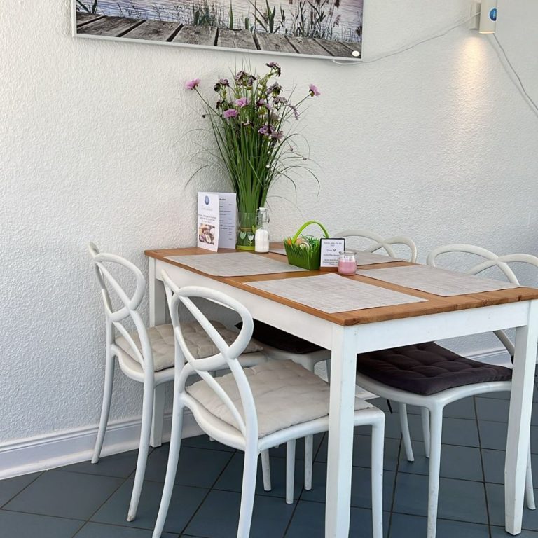 Café Fehmarn, Insel-Kaffeeklatsch Fehmarn Heller Tisch mit weißen Stühlen und Blumenvasen in einem modernen Raum.