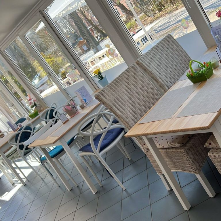 Café Fehmarn, Insel-Kaffeeklatsch Fehmarn Helle, einladende Café-Umgebung mit Tischen und Stühlen aus Rattan und Holz.