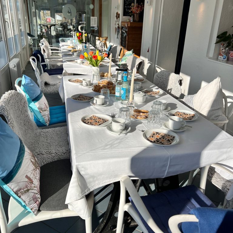 Café Fehmarn, Insel-Kaffeeklatsch Fehmarn, Trauercafé Tisch gedeckt mit Kaffeetassen, Gebäck und Blumen in einer hellen Umgebung.